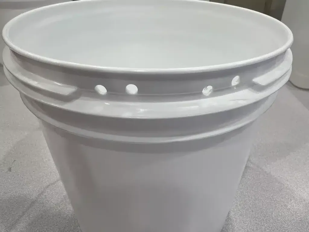 A plain white 5-gallon plastic bucket with holes drilled near the rim, empty and unmounted — the starting material before it is fitted with zip ties for a DIY crate water bucket.