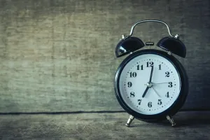 A black twin-bell analog alarm clock with a white face sits on a rustic wooden surface.
